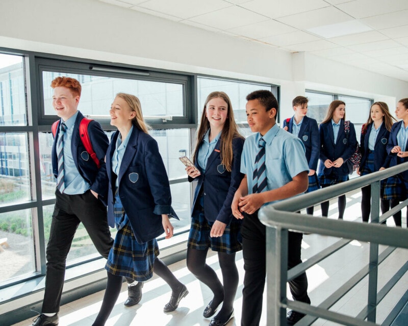 A group of co-ed secondary school students walking along a corridor.