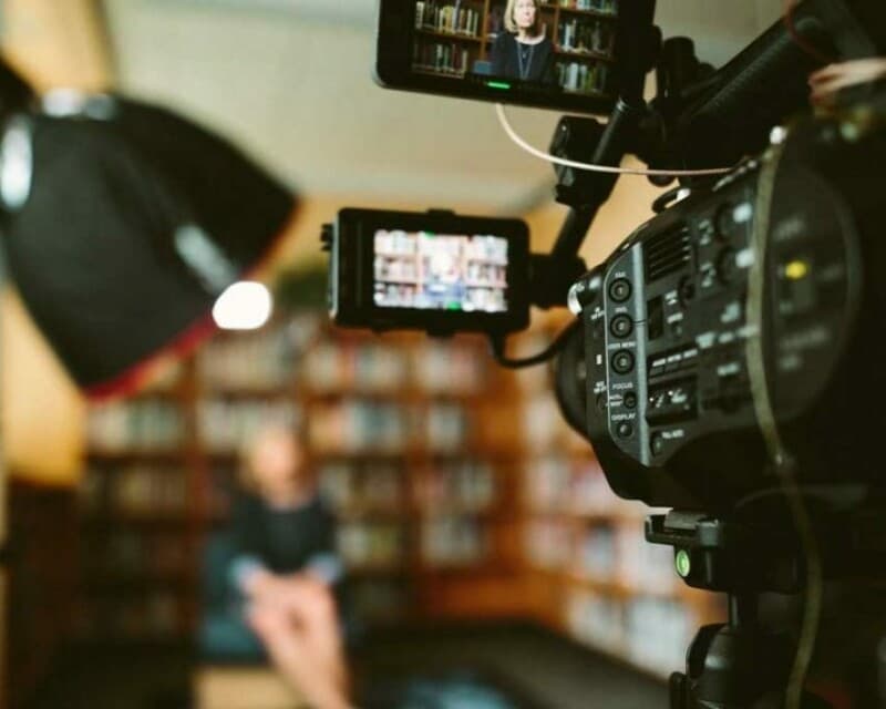 Interview being recorded with subject in view of a camera, we are behind the camera.