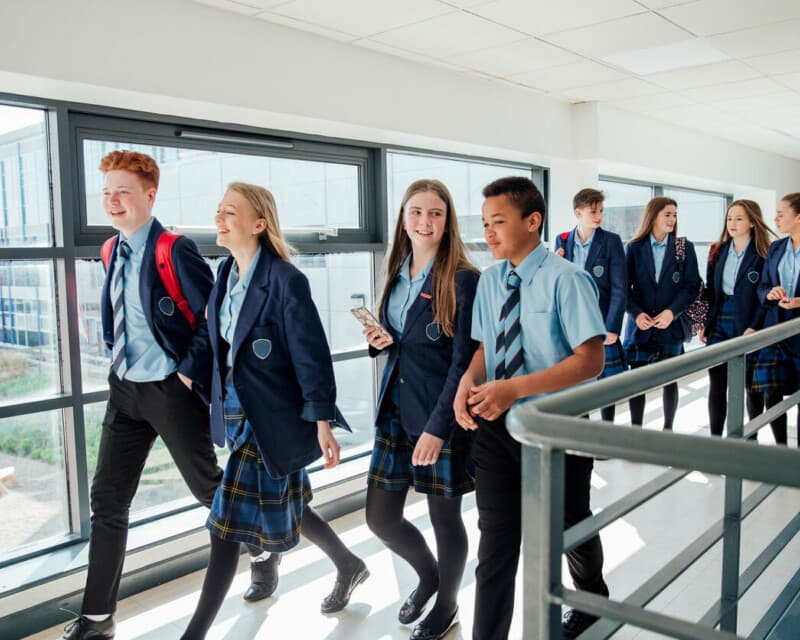 A group of co-ed secondary school students walking along a corridor.
