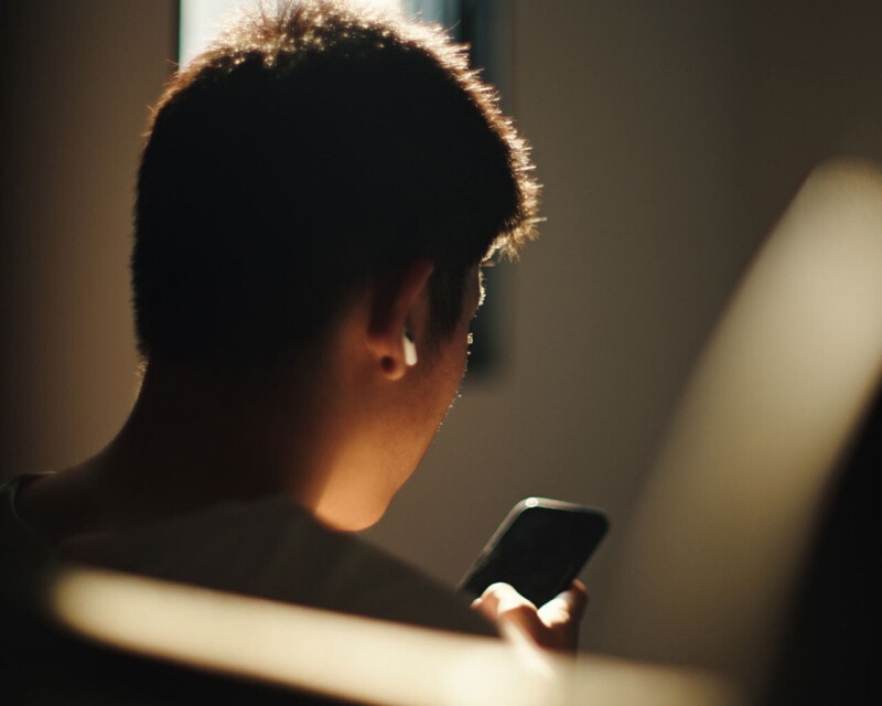 Person sitting indoors and looking at a mobile phone illuminated by the screen's light.