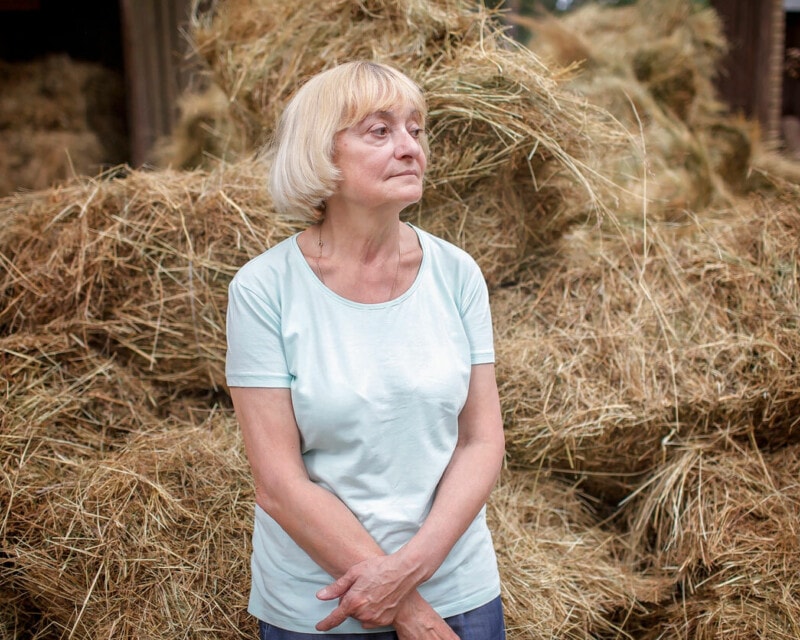 Older woman in front of a haystack looking thoughtfully away from camera.