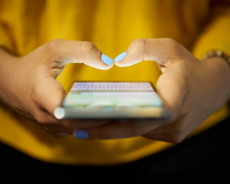Young woman using cell phone to send text message on social network at night.